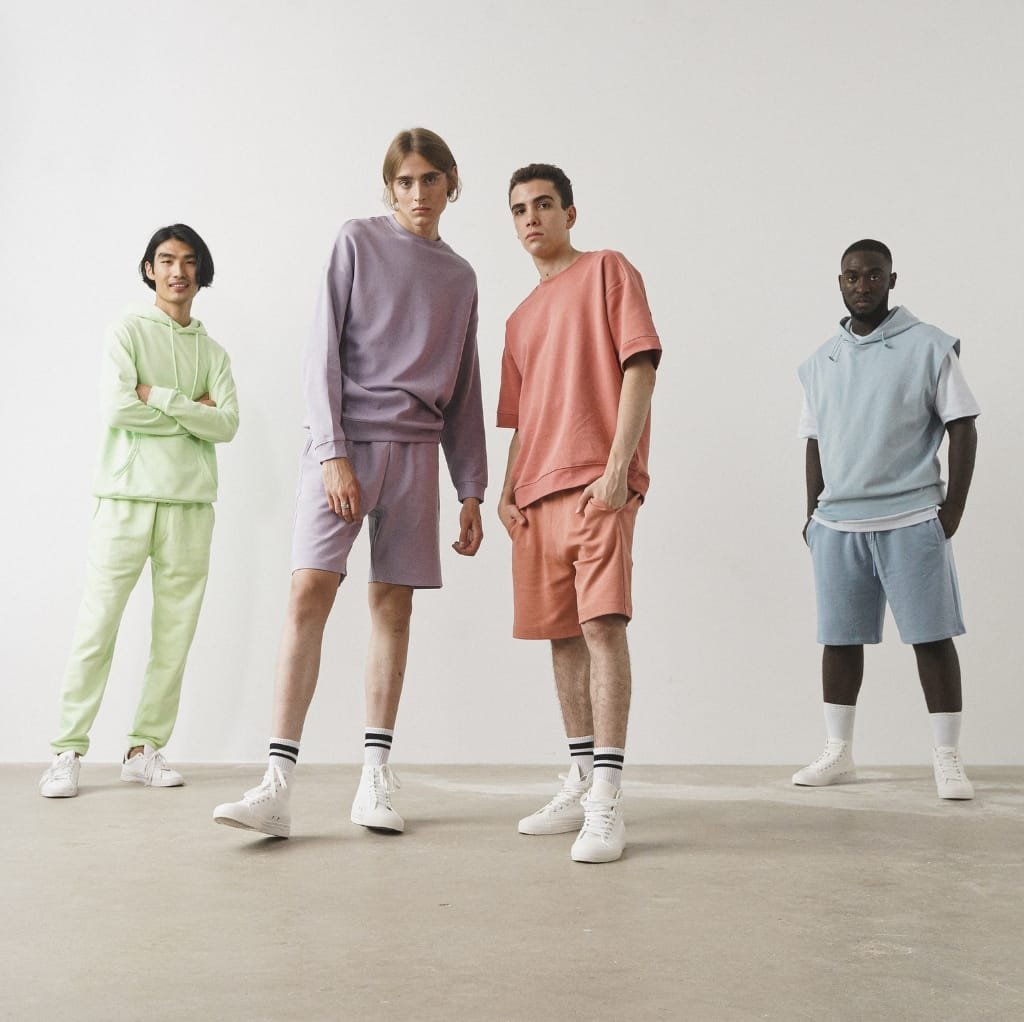 A diverse group of four young adults dressed in colorful, casual streetwear outfits, standing against a plain white background.