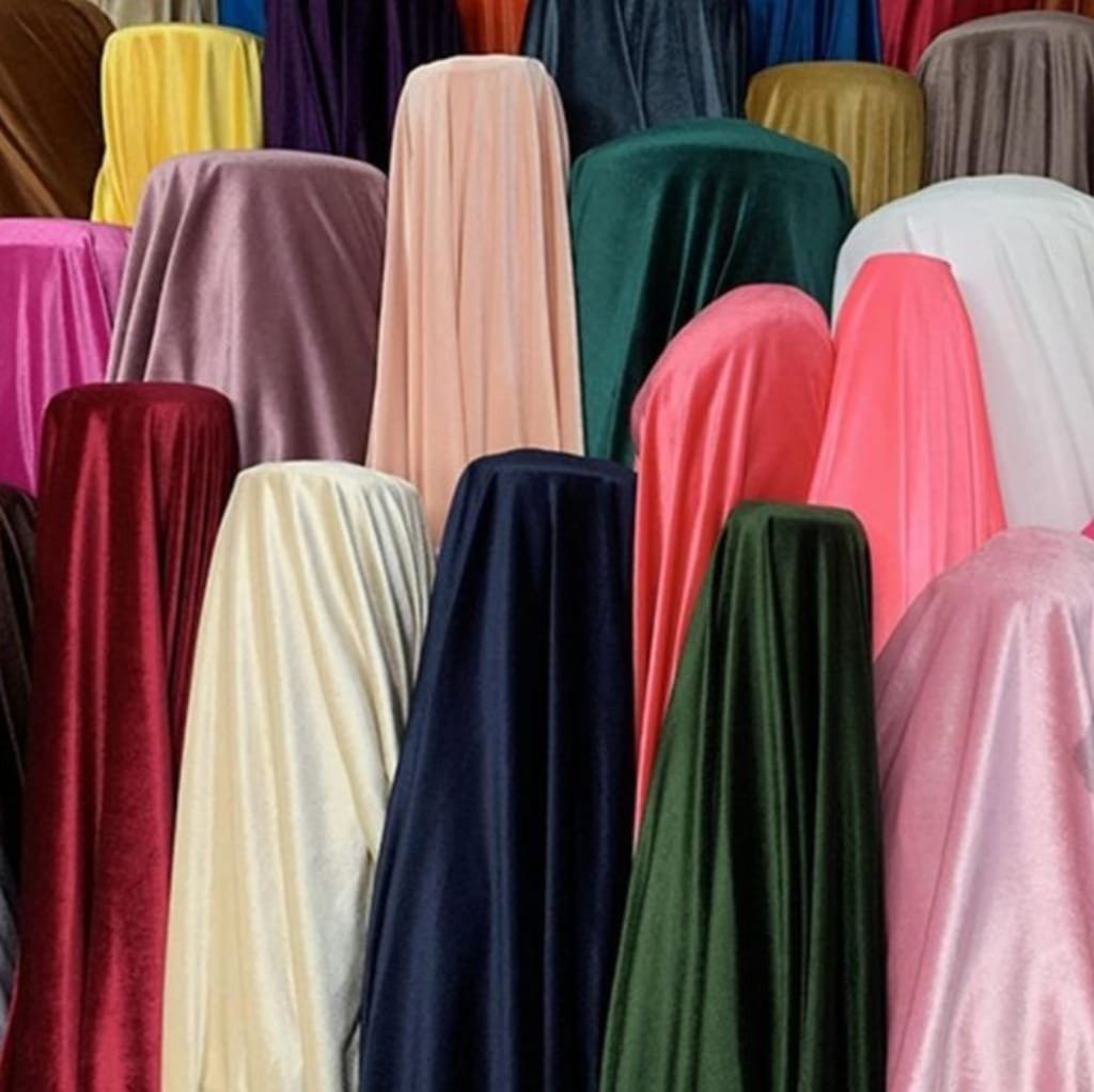A variety of velvet and velour fabric swatches in different vibrant colors, including pink, yellow, purple, green, navy blue, cream, and red, arranged in a display.