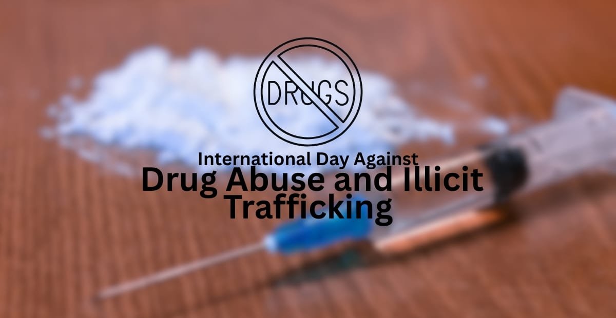 A syringe lying on a wooden surface with some white powder in the background, overlaid with a "No Drugs" symbol and the text "International Day Against Drug Abuse and Illicit Trafficking."