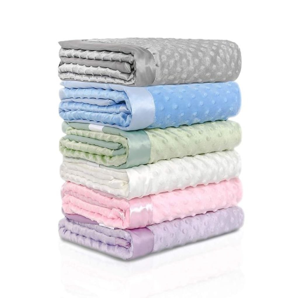 A neatly stacked pile of colorful, soft minky fabric blankets in shades of gray, blue, green, white, pink, and lavender, each with a textured, dotted surface.