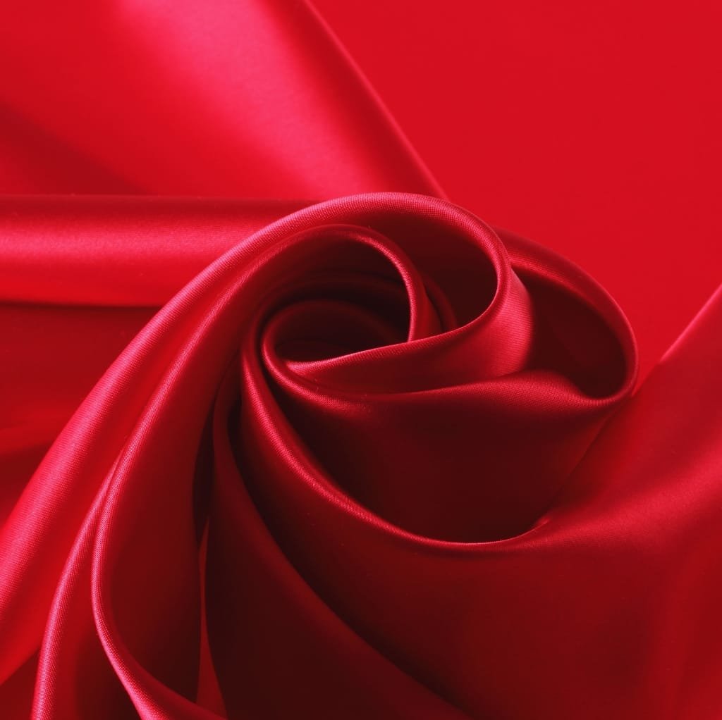 A close-up image of vibrant red satin-woven cotton fabric, showcasing its smooth, glossy surface and luxurious texture.