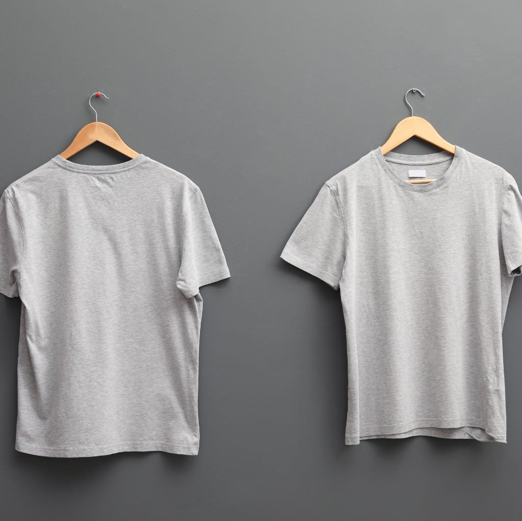 Two light gray T-shirts hanging on wooden hangers against a gray wall, with one T-shirt layered over the other to add visual depth.