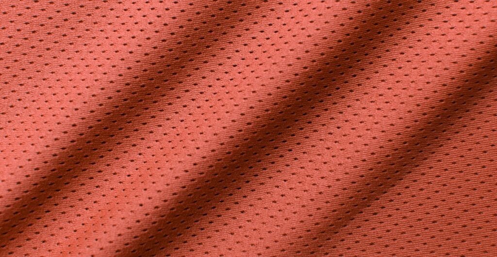 Close-up image of red mesh spandex fabric showing its perforated, breathable texture with small black dots.