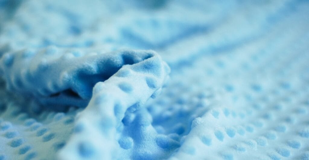 Soft, plush light blue fabric with a textured, dimpled surface and a rolled-up section in the foreground.