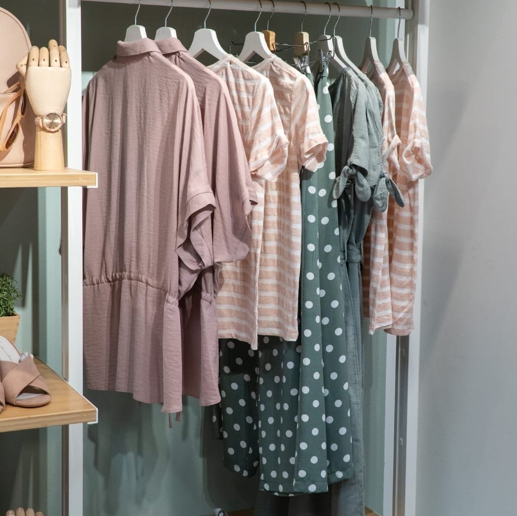 A display of various maxi cotton dresses hanging in a clothing store, featuring soft pastel and checkered patterns in shades of pink, green, and peach.