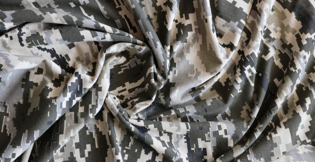 A piece of fabric with a digital camouflage pattern in shades of black, grey, and white, draped with soft folds and curves.