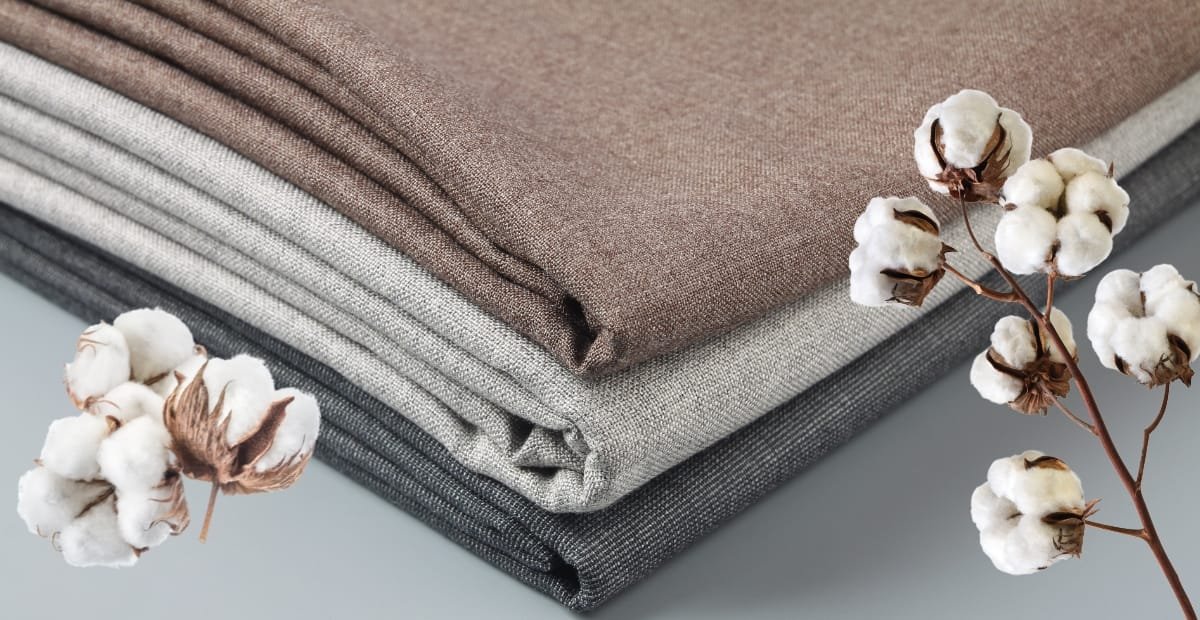Three neatly folded pieces of fabric in shades of brown, beige, and gray with cotton branches placed beside them.