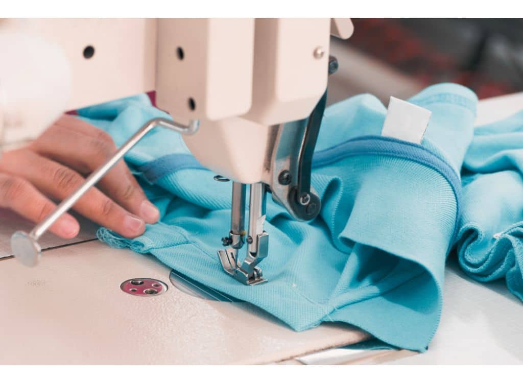 Close-up of a sewing machine stitching a light blue polo shirt with a focus on the fabric and sewing details.