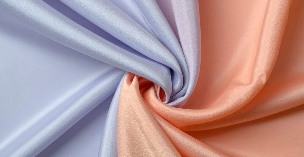 Close-up of pastel-colored chiffon fabric in lavender and peach, gently gathered and twisted to showcase its silky texture.