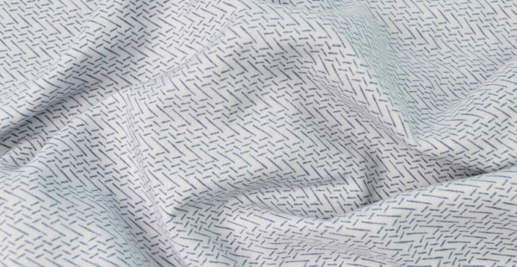 Close-up image of light-colored Sea Island cotton fabric with fine, small, dark dashed lines forming a subtle, intricate pattern.
