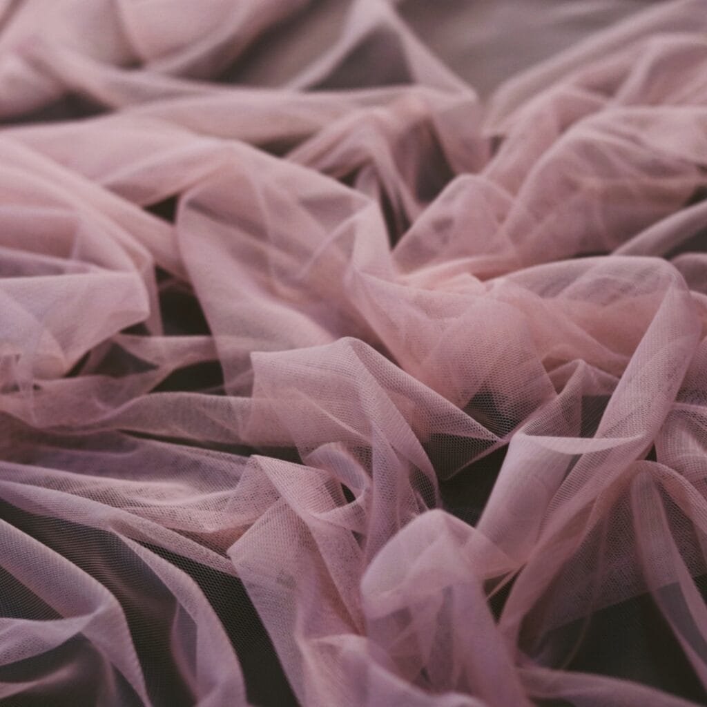A close-up view of soft, pink, sheer fabric ruffles with a delicate and flowing texture.