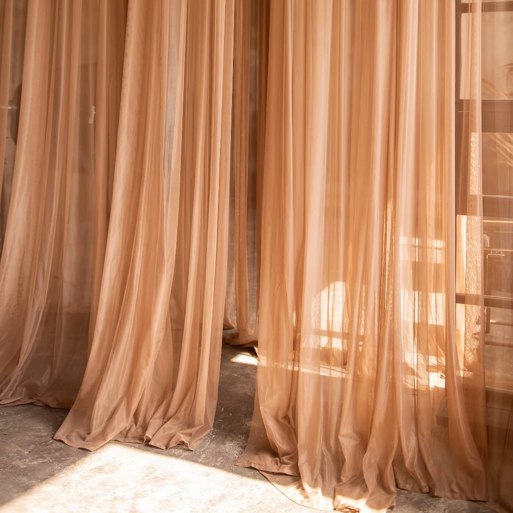Sheer beige curtains gathered and draped, allowing light to filter through, creating a warm atmosphere.