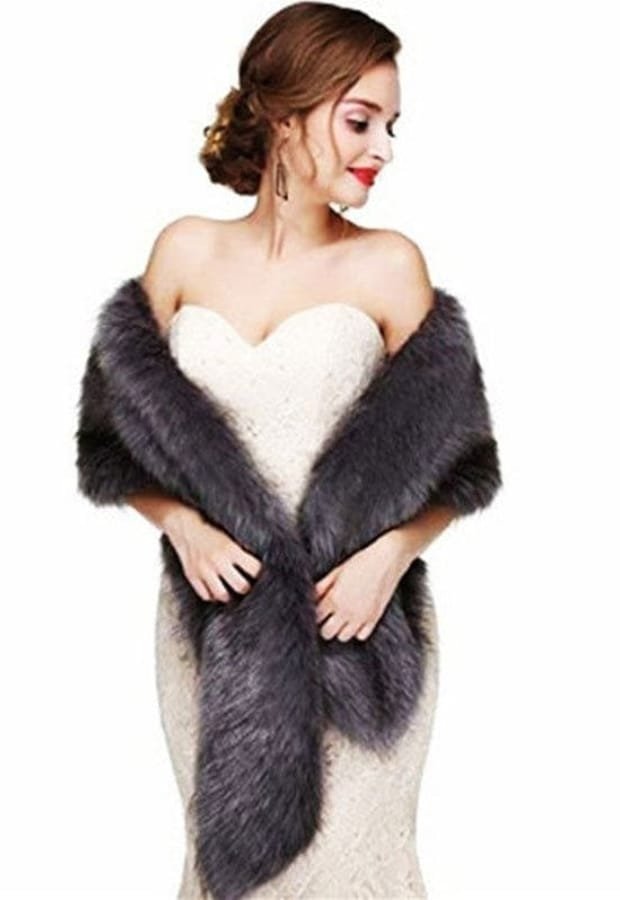 Elegant woman in a strapless white lace dress, draped in a luxurious dark gray fur stole or wrap, styled against a plain white background.