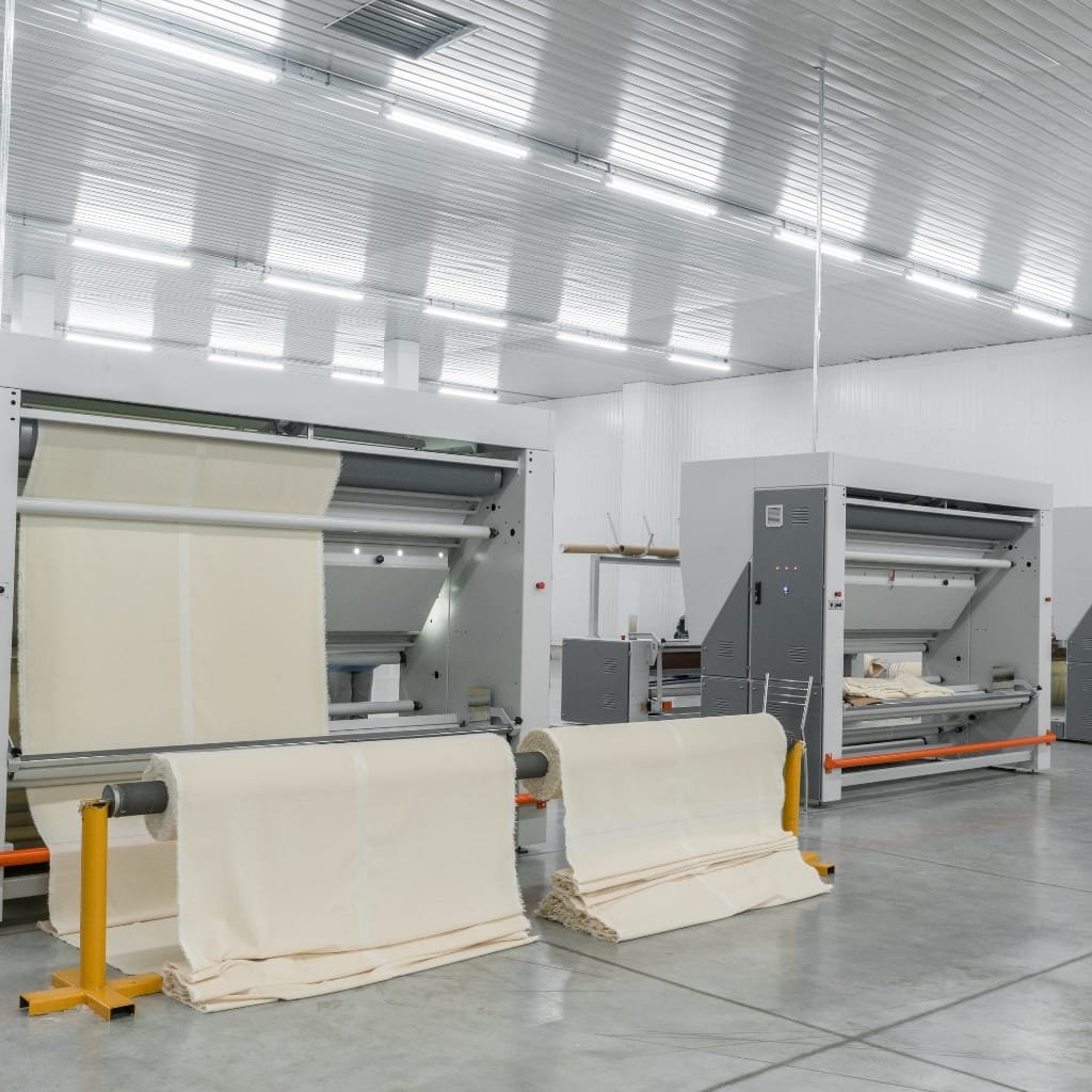 Bright, modern manufacturing facility with large automated machines producing and handling rolls of white fabric.