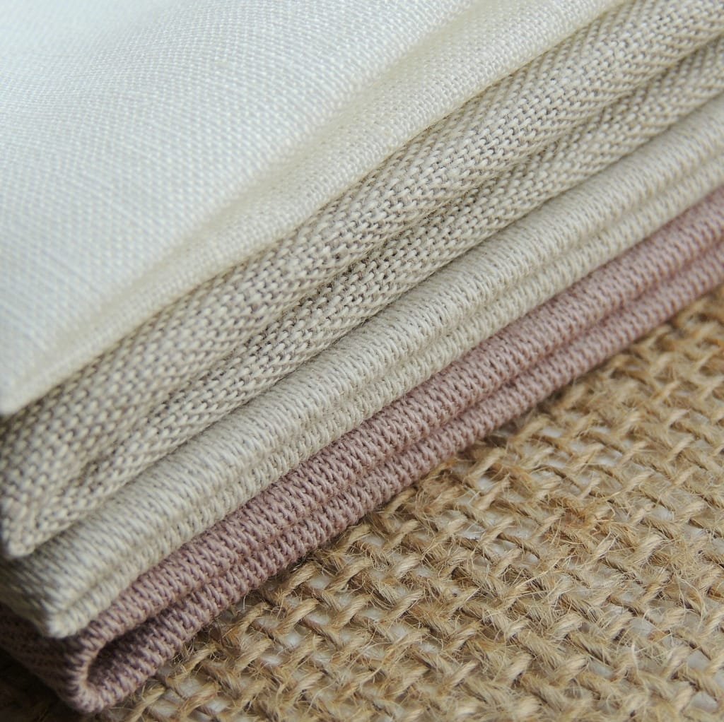 Close-up image of neatly folded woven cotton fabrics in neutral tones, showcasing their textured weave and natural fibers.