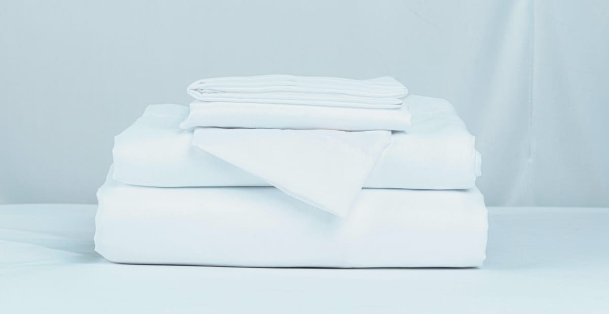 A neatly folded stack of white bed linens on a light blue background.