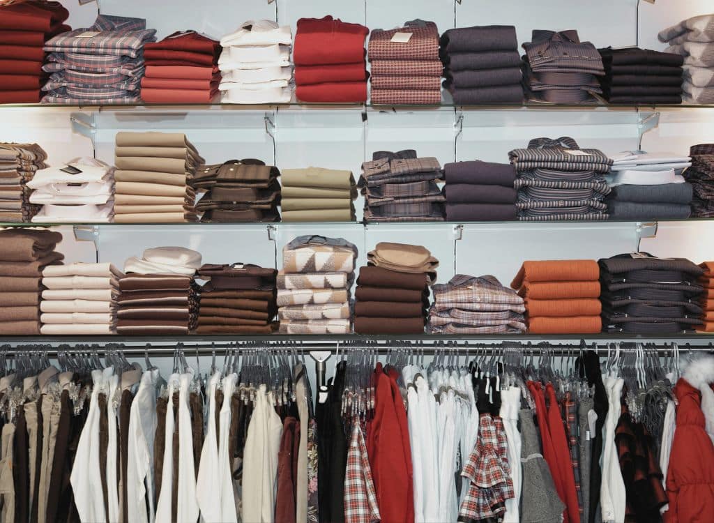 Shelves stacked with folded sweaters and shirts in various colors, alongside hanging garments including coats and dresses, showcasing a collection of clothing items from a manufacturer in Delaware.