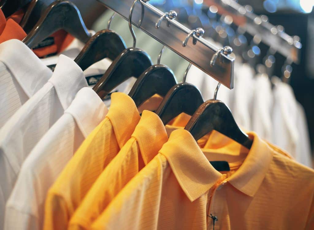 A collection of customized polo shirts in white and orange, neatly hanging on wooden hangers.
