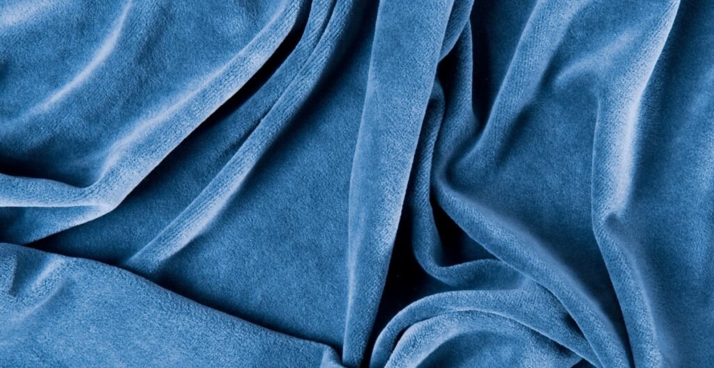 Close-up image of soft, blue velour fabric with gentle folds and a plush texture.