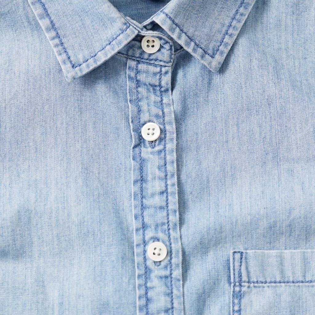 Close-up of a light blue chambray shirt with a button-down collar, showing the fabric texture and buttons.