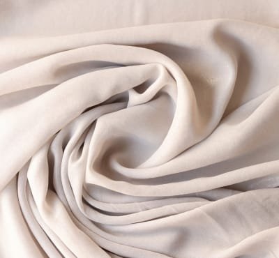 A close-up image of soft, flowing, cream-colored fabric with a smooth and slightly shiny surface, showcasing the luxurious texture of cotton-silk fabric.