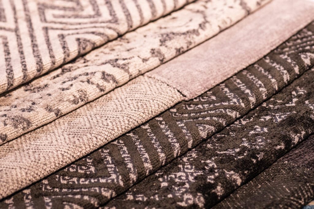 Close-up image of multiple rolls of patterned cotton weaving fabric in shades of beige, pink, and brown.