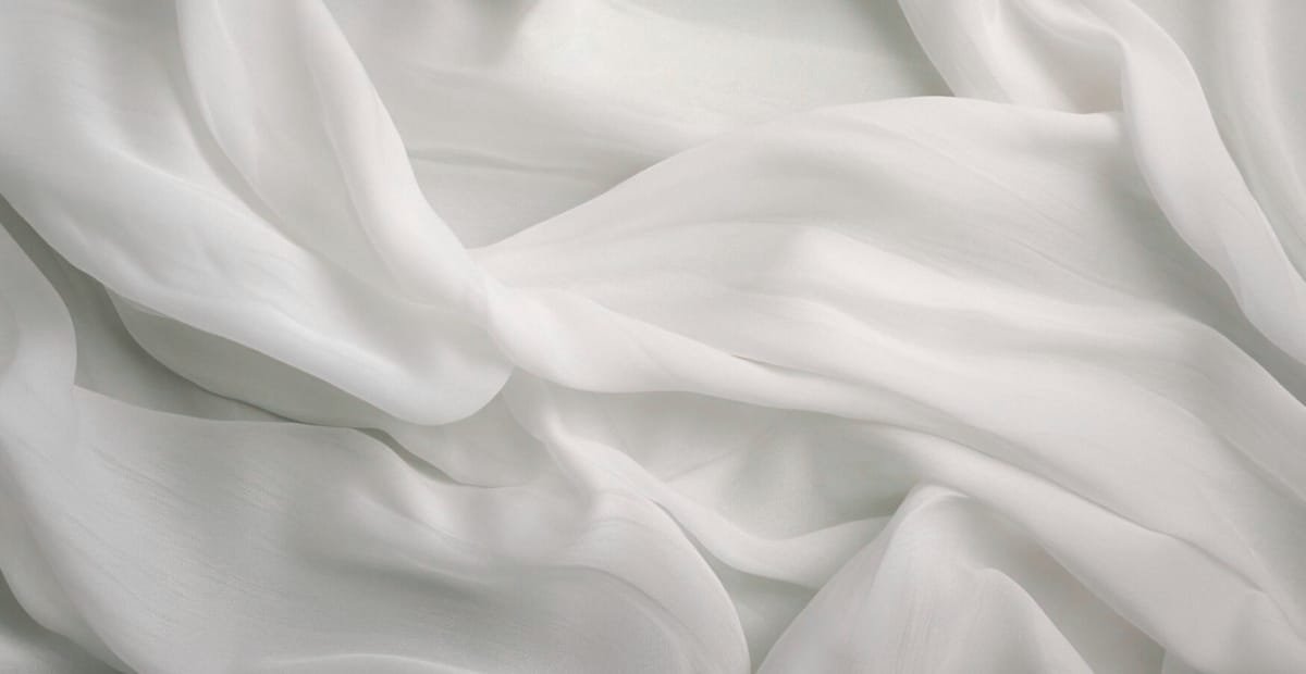 Close-up image of soft, flowing white chiffon fabric with gentle folds and a delicate, lightweight appearance.