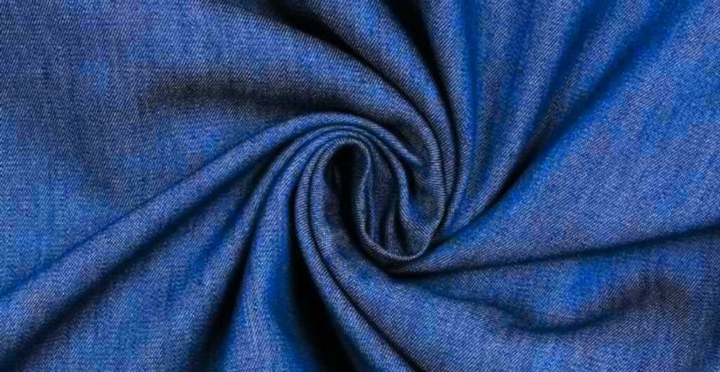 Close-up image of a piece of denim chambray fabric twisted into a swirl, showcasing its texture and blue color.