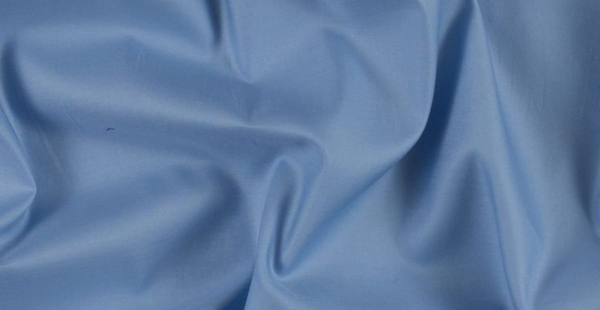 Close-up image of smooth, light blue Egyptian cotton fabric with gentle folds.