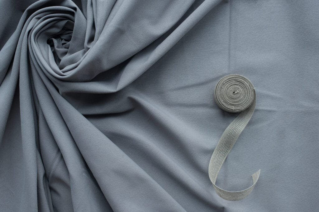 A close-up image of soft, grey Egyptian cotton fabric with a roll of matching fabric trim placed on top.