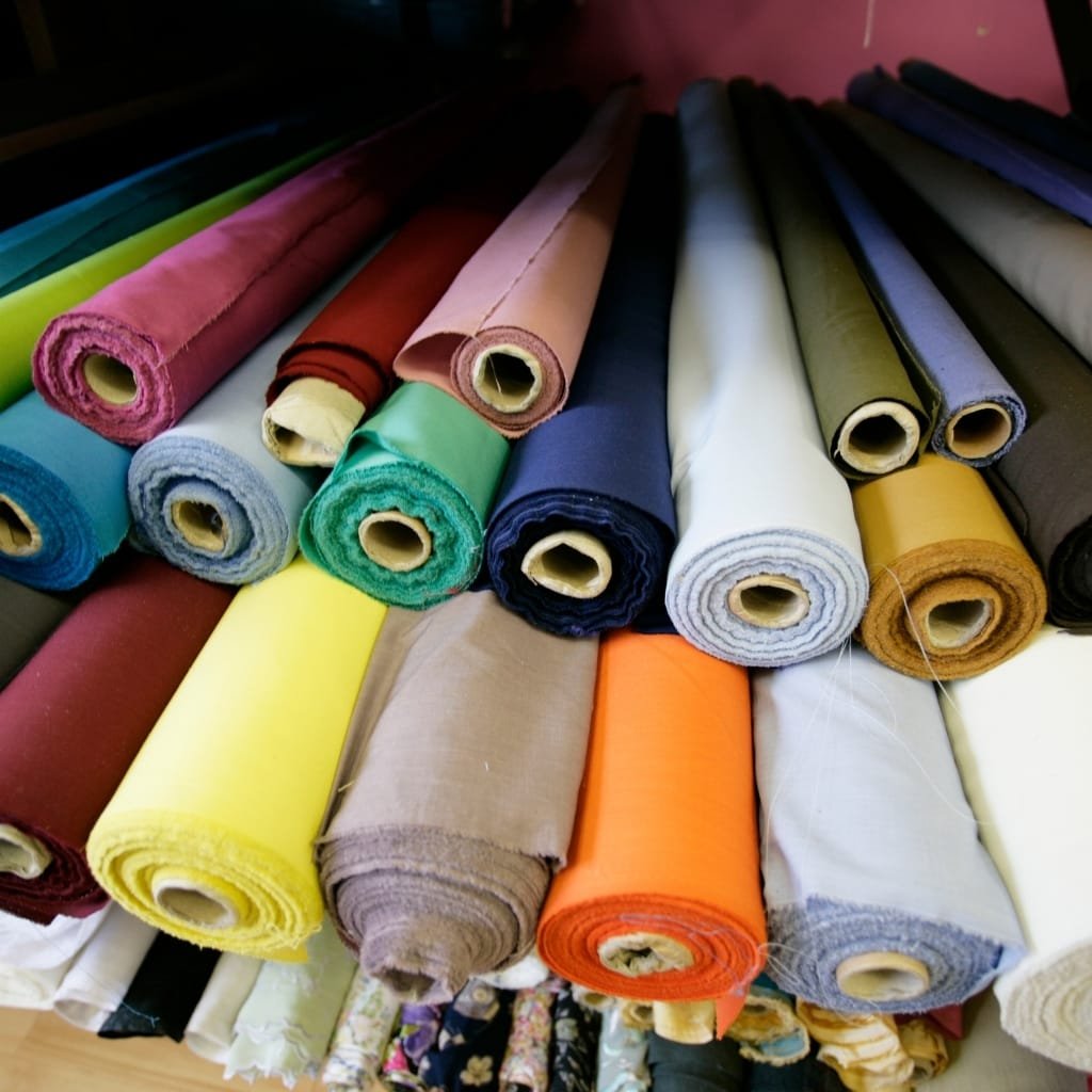 A collection of colorful fabric rolls arranged on a table, displaying various shades including pink, green, yellow, beige, orange, white, black, and dark blue.