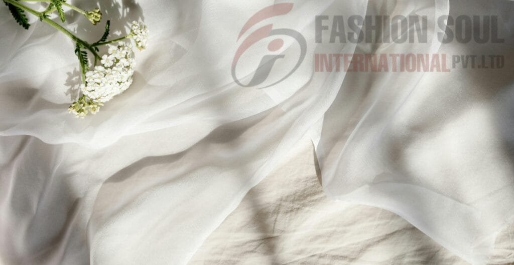 A close-up of white fabric with delicate white flowers and green stems resting on it, with a semi-transparent logo of "Fashion Soul International Pvt Ltd" in the background.