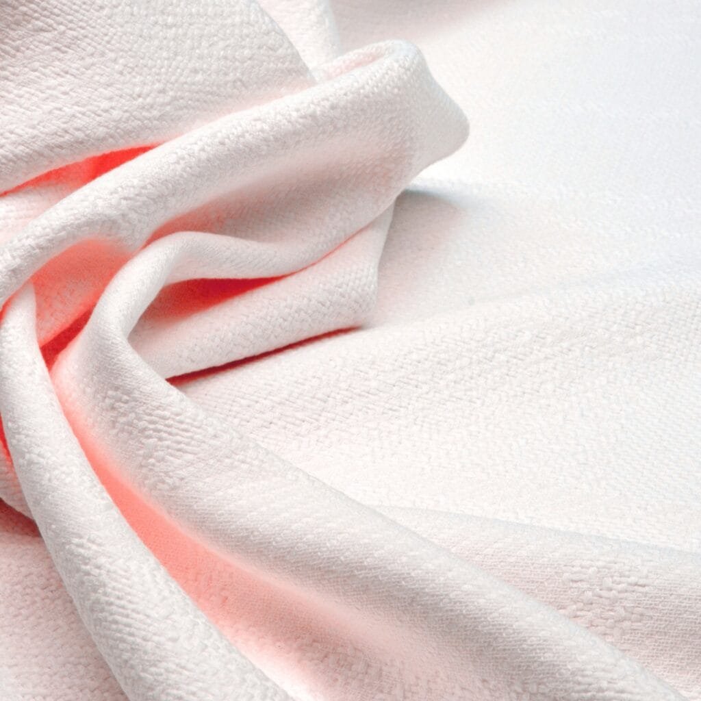 Close-up image of a piece of white long-staple cotton fabric with a soft and smooth texture, gently gathered with some light pink fabric underneath.