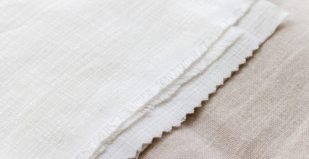 Close-up of a piece of plain weave cotton fabric, showing the tight, evenly woven texture and frayed edge.