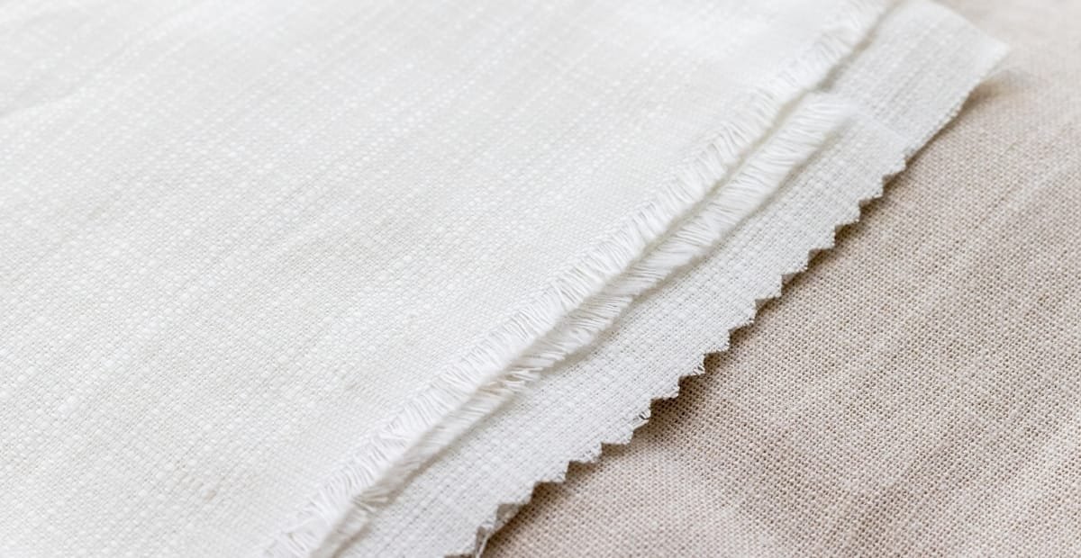 Close-up of a piece of plain weave cotton fabric, showing the tight, evenly woven texture and frayed edge.