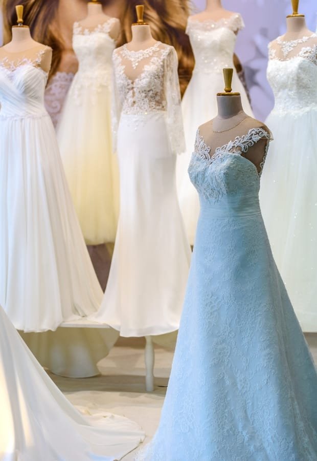 A display of elegant prom dresses on mannequins, featuring various styles in white and ivory, with lace, chiffon, and satin fabrics, set against a softly lit background.