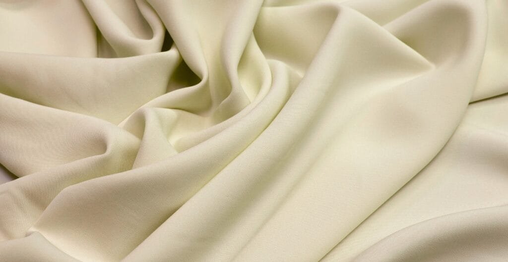 Close-up image of soft, cream-colored rayon spandex fabric with gentle folds.