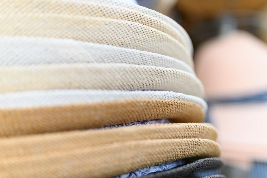 Close-up of stacked plain weave cotton fabric in various natural and neutral colors, showcasing the texture and weave pattern.