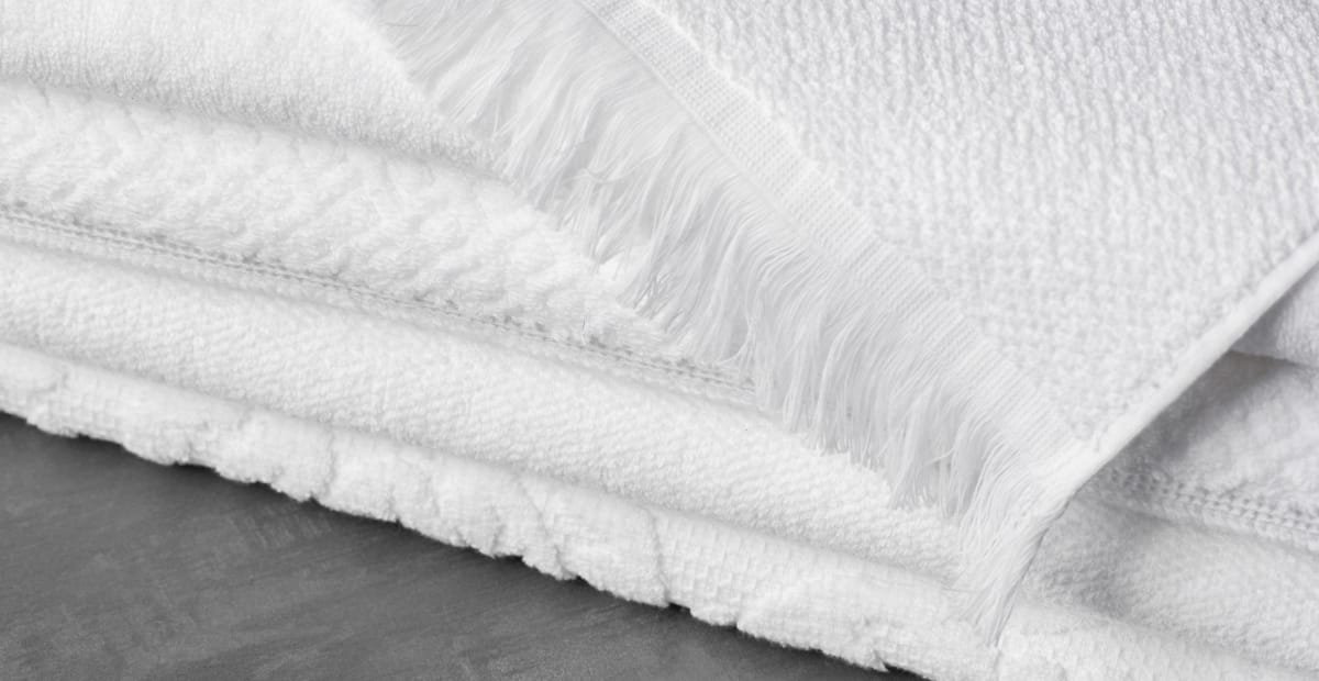Close-up of thick white cotton fabric with a textured surface and fringed edges, folded over a grey surface.