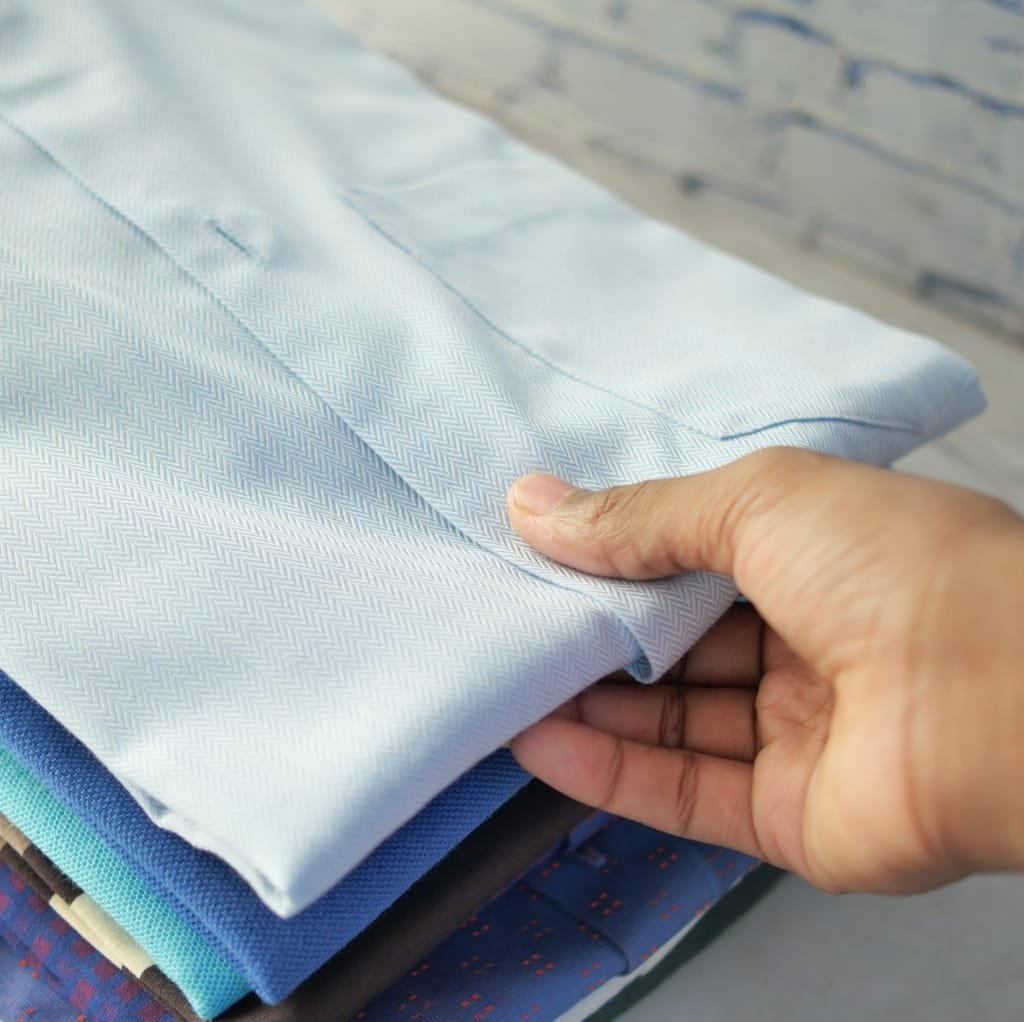 A close-up image of a person holding a neatly folded piece of light blue twill weave cotton fabric, showing its smooth texture and fine diagonal pattern.
