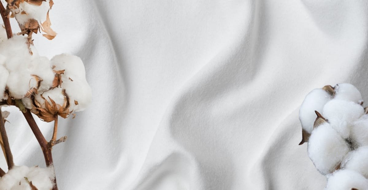 Soft, pristine white cotton fabric with a smooth, slightly wrinkled texture, garnished with cotton boll branches on either side.