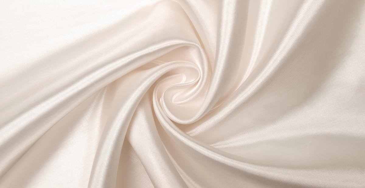 Close-up view of smooth, cream-colored silk organza fabric with a swirling pattern.