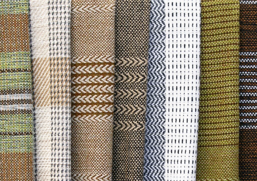 Close-up image of a variety of cotton weave fabrics with different patterns and colors, including checkered, striped, zigzag, grid, and textured designs.