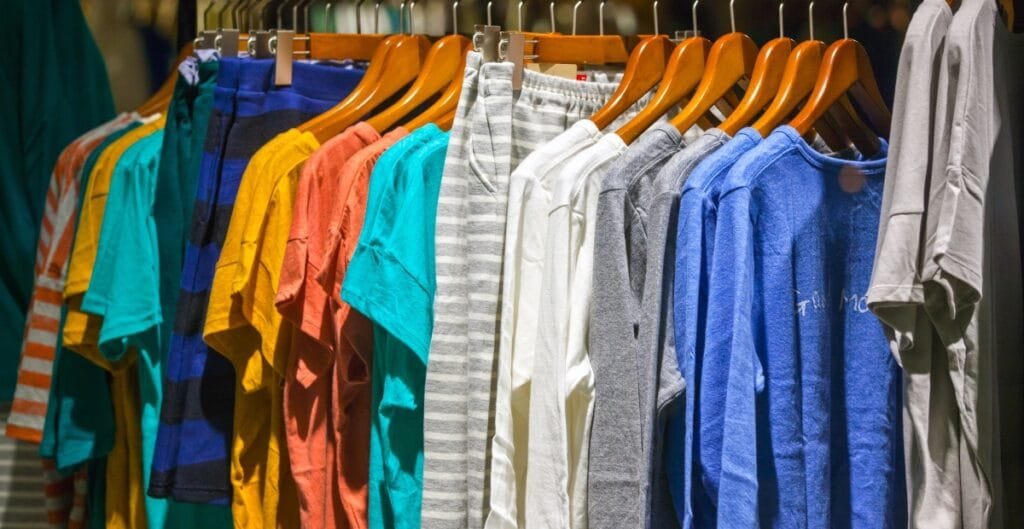 A retail clothing rack featuring a variety of men's T-shirts in multiple colors and patterns, hanging on wooden hangers.
