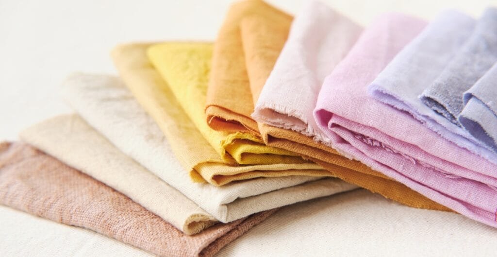 A neatly folded stack of colorful fabric cloths in pastel shades including yellow, beige, orange, pink, and lavender.