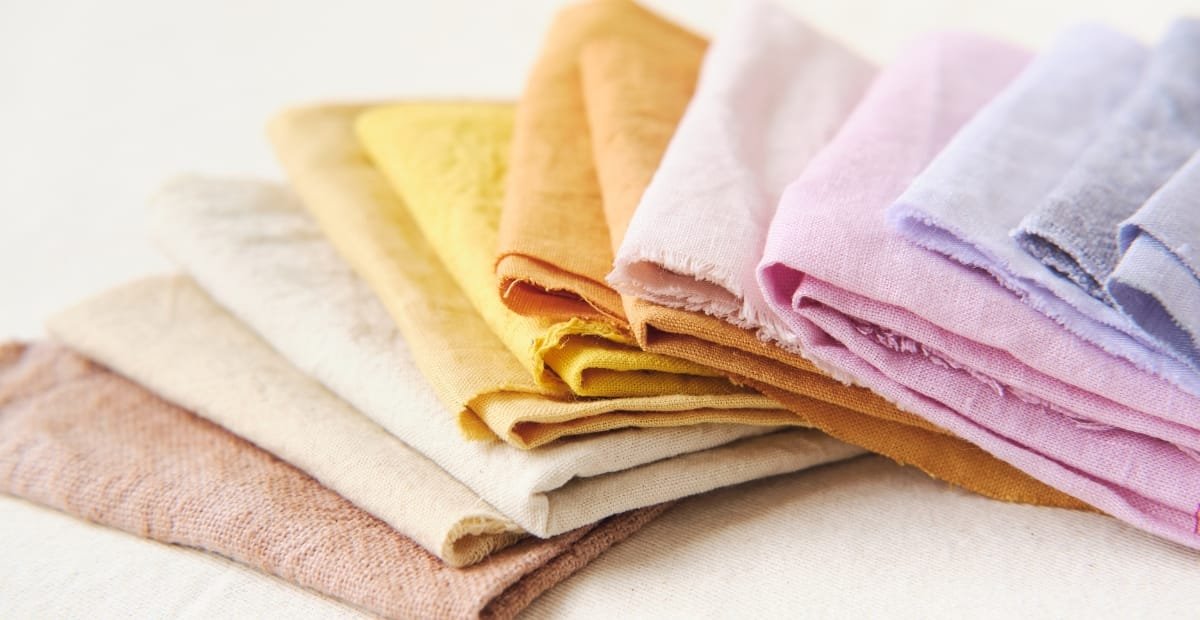 A neatly folded stack of colorful fabric cloths in pastel shades including yellow, beige, orange, pink, and lavender.