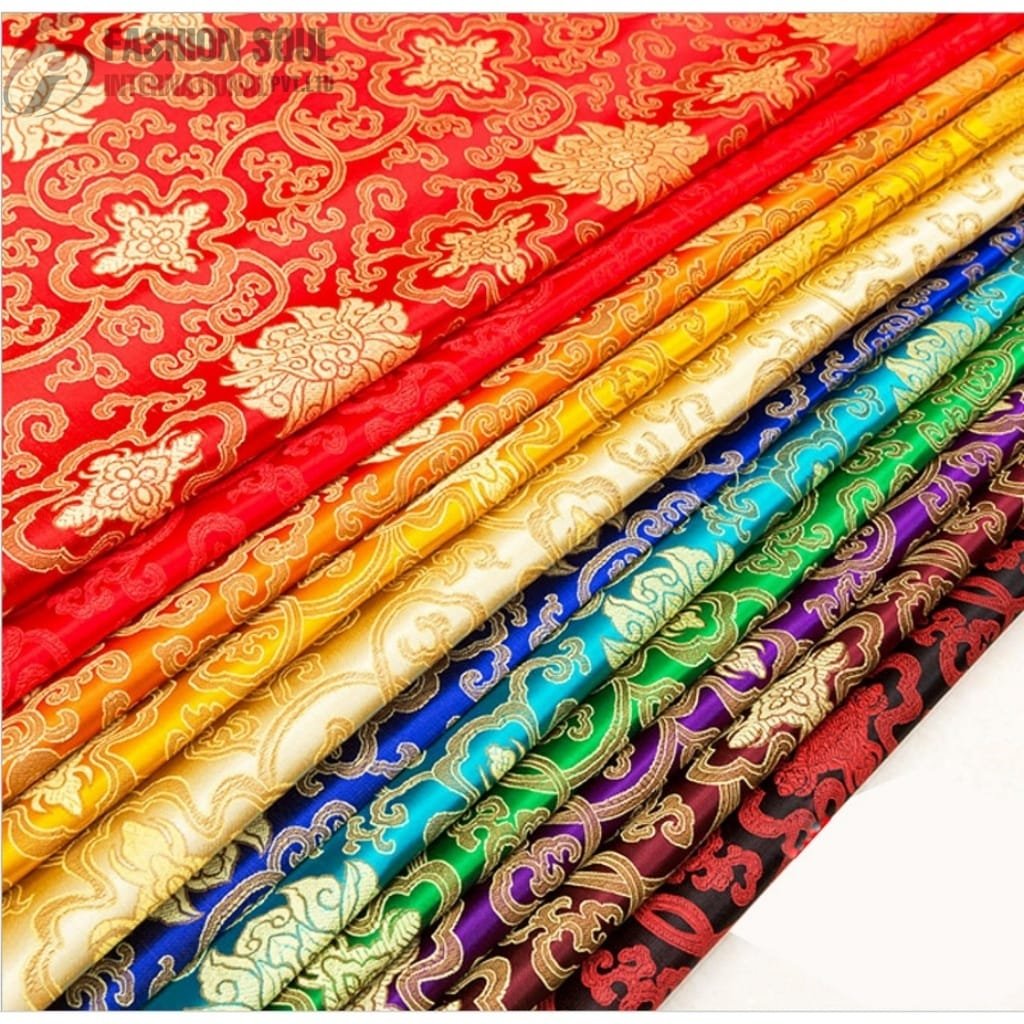 A collection of colorful, intricately patterned silk fabrics arranged in a diagonal row. The fabrics feature traditional floral and swirling designs in various vibrant colors, including red, orange, yellow, blue, green, purple, and black, all accented with gold detailing.