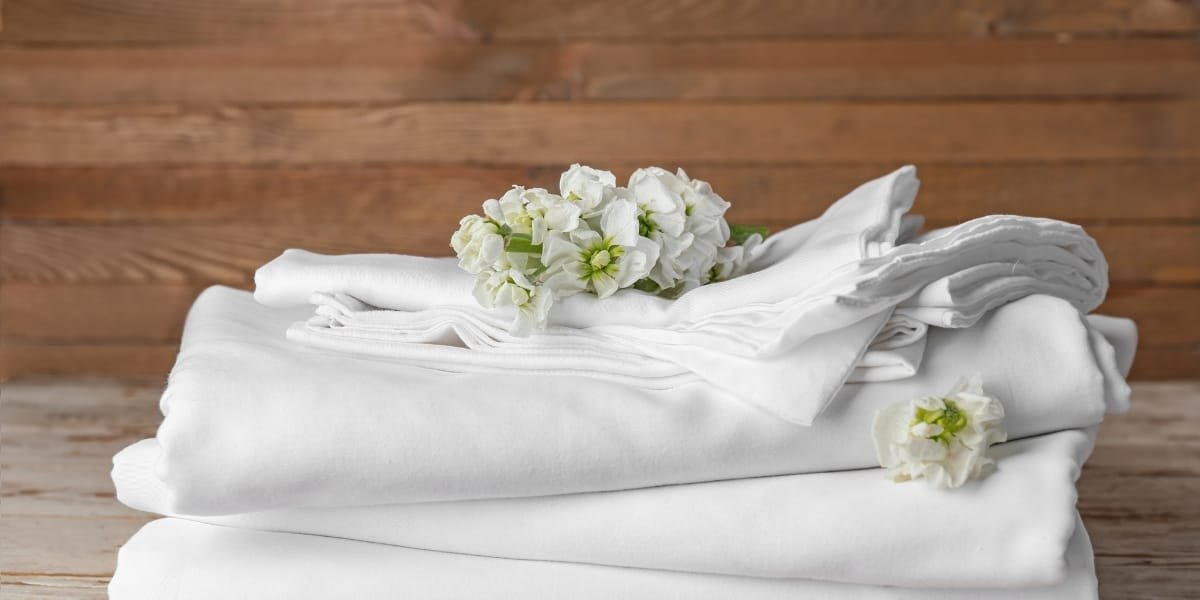 A neatly arranged stack of white towels with white flowers on top, set against a wooden background.