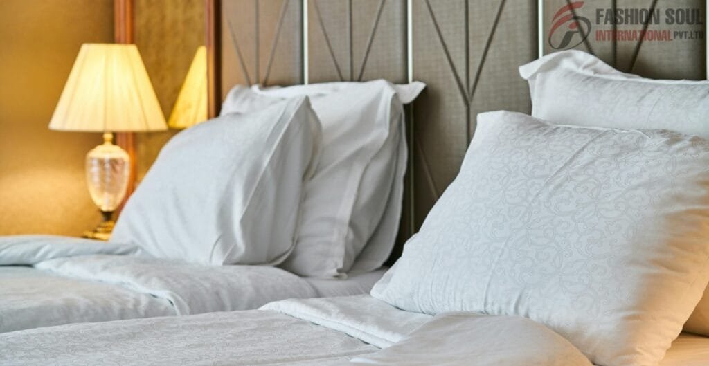 Close-up of a neatly made bed with white pillows and bed linens, a bedside lamp with a beige lampshade, and a wooden headboard in a warmly lit room.