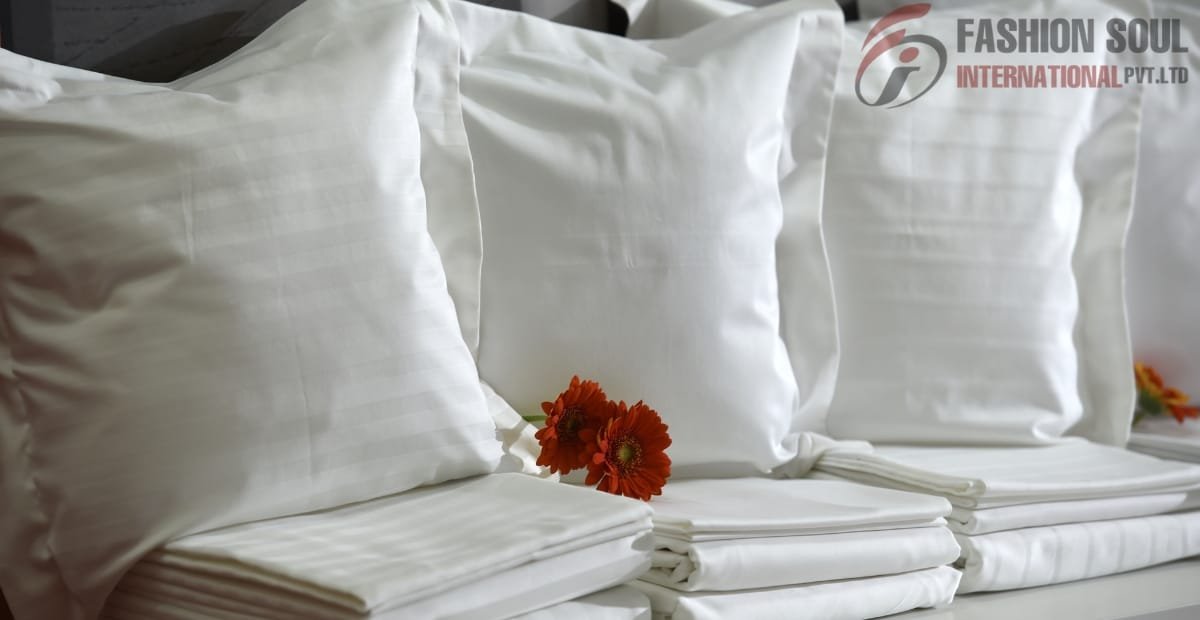 A neatly arranged set of white satin pillowcases and bedsheets with a small orange flower placed between them, on a bed or display surface.
